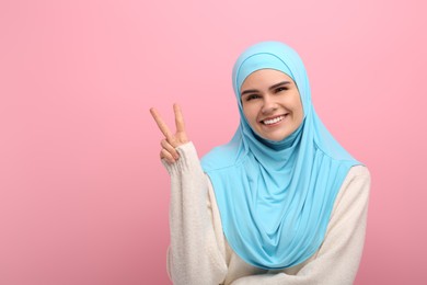 Photo of Muslim woman in hijab showing V-sign on pink background, space for text