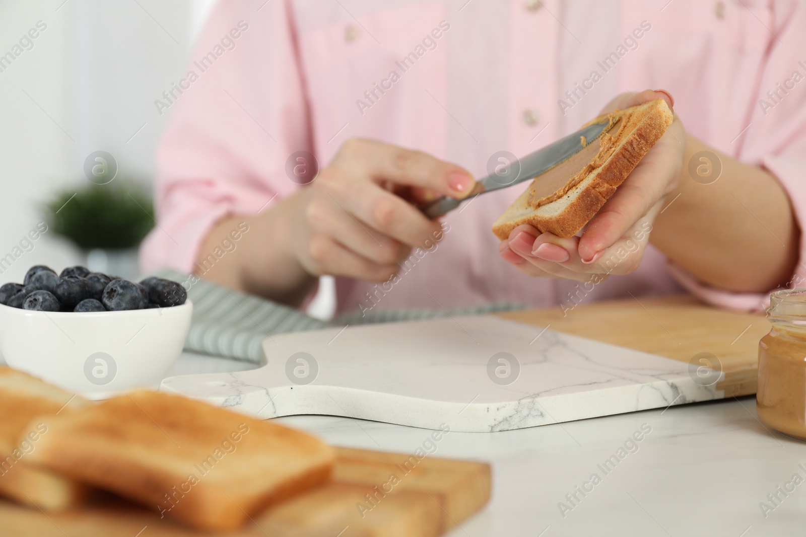 Photo of Woman spreading tasty nut butter onto toast at white table, closeup