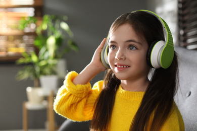 Photo of Cute little girl with headphones listening to audiobook at home