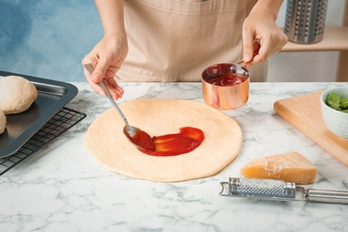 Photo of Woman spreading tomato sauce on pizza on table