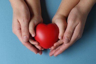 Mother and her child holding red decorative heart on light blue background, top view