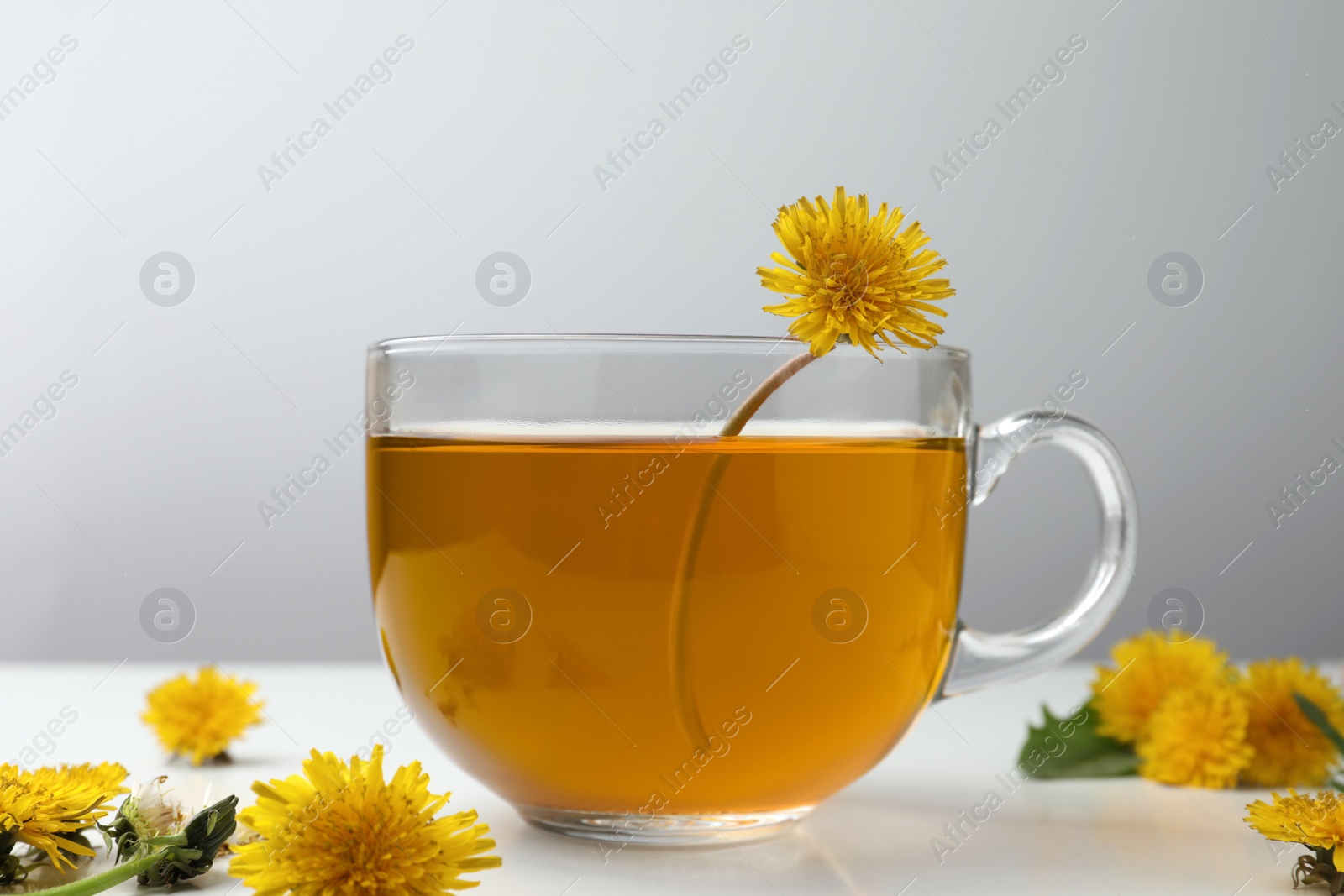 Photo of Delicious fresh tea and beautiful dandelion flowers on white table