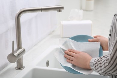Woman wiping plate with paper towel above sink in kitchen, closeup