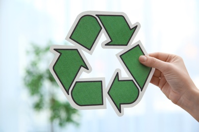 Woman holding recycling symbol on blurred background, closeup