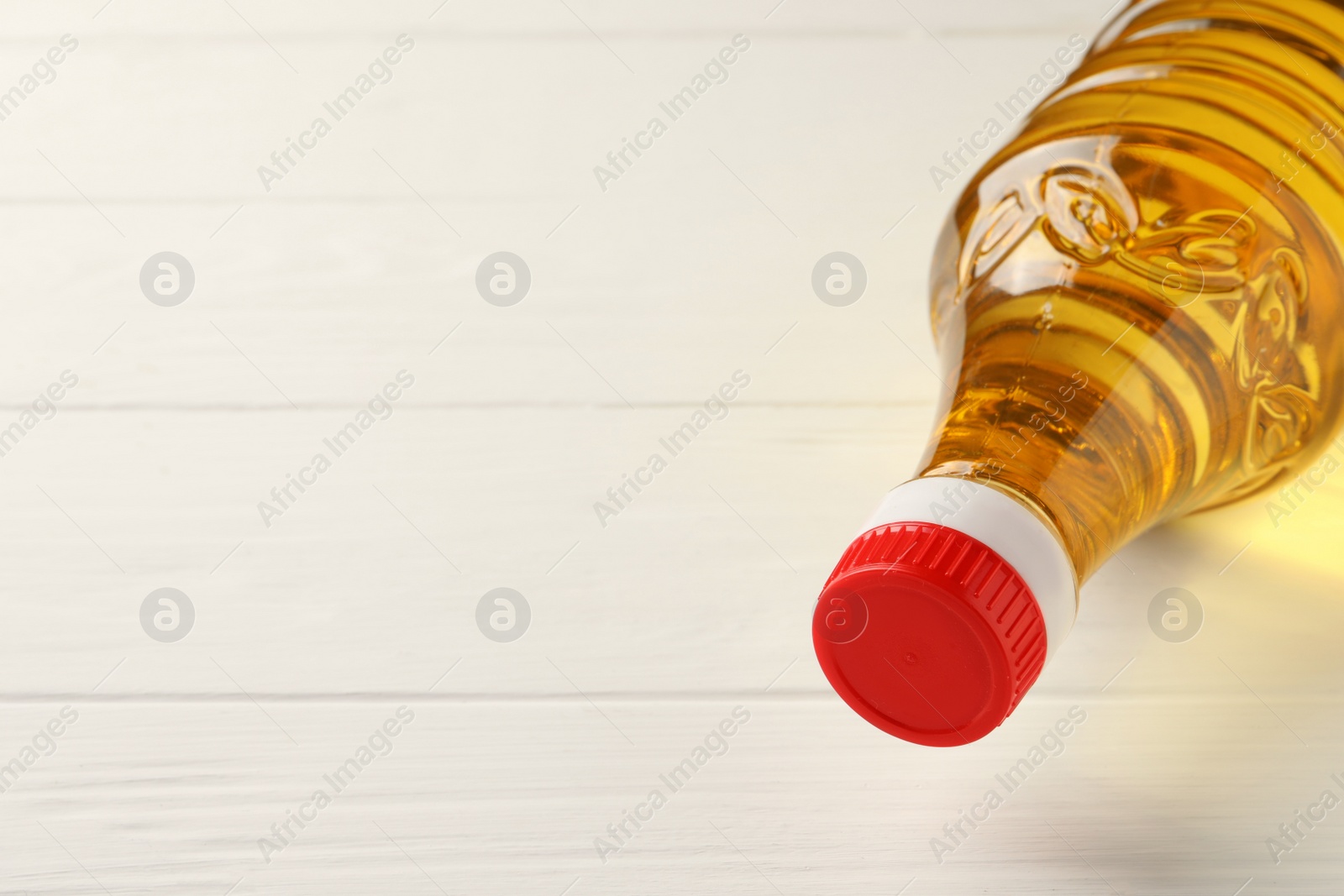 Photo of Plastic bottle of cooking oil on white wooden table, space for text