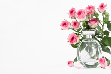 Photo of Bottle of luxury perfume and beautiful roses on white background, space for text. Floral fragrance