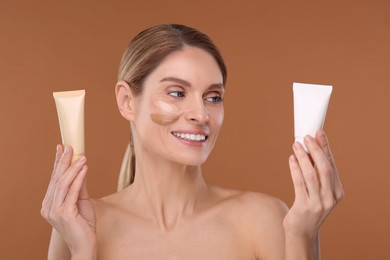 Woman holding tubes of foundation on brown background