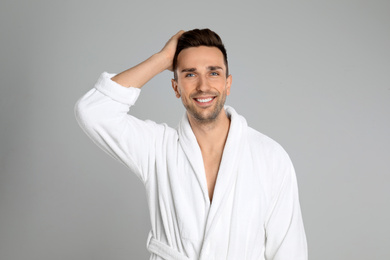 Happy young man in bathrobe on light grey background