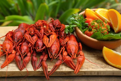 Photo of Delicious red boiled crayfish and products in bowl on wooden table