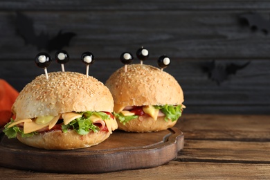 Photo of Cute monster burgers served on wooden table, space for text. Halloween party food