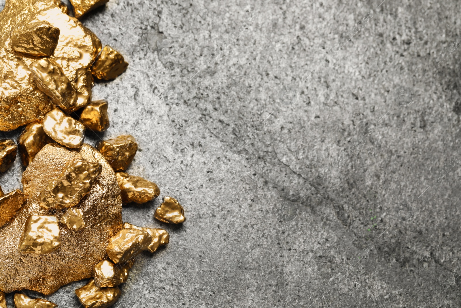 Photo of Pile of shiny gold nuggets on grey table, flat lay. Space for text