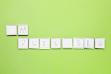 Photo of Motivation concept. Changing word from Impossible into Possible by removing paper on light green background, flat lay