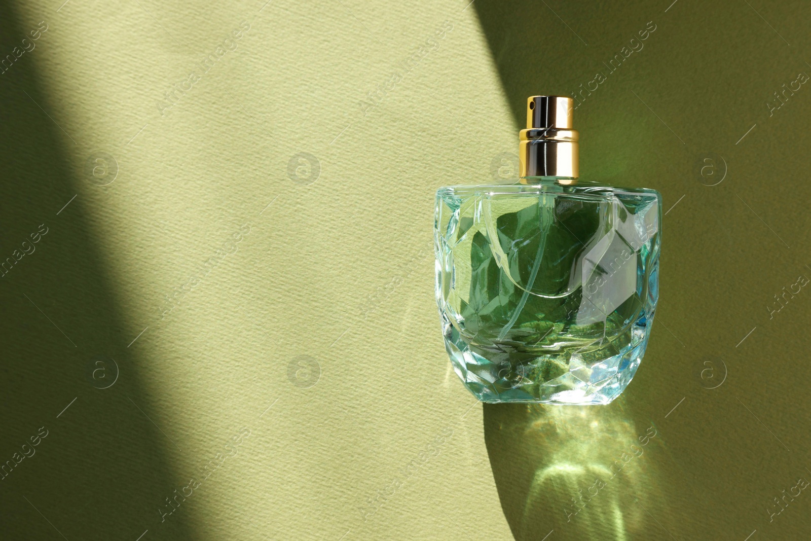 Photo of Luxury women's perfume. Sunlit glass bottle on olive background, top view. Space for text