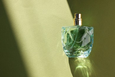 Luxury women's perfume. Sunlit glass bottle on olive background, top view. Space for text