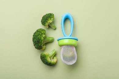 Photo of Nibbler with boiled broccoli on green background, flat lay. Baby feeder