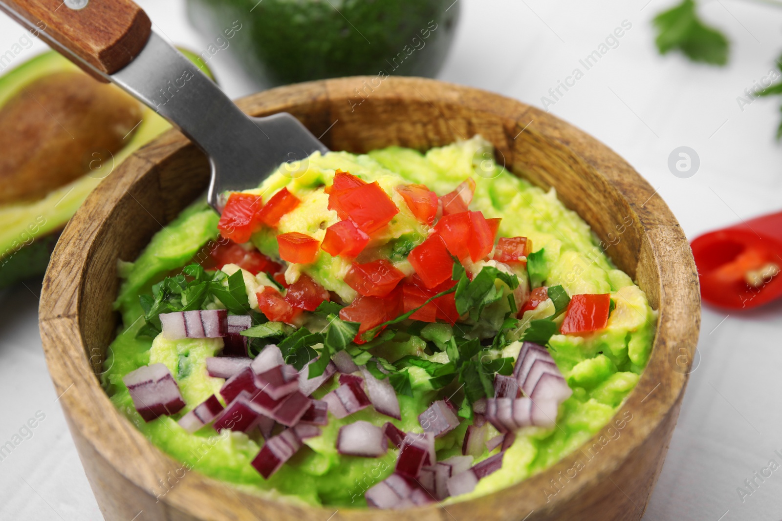 Photo of Bowl of delicious guacamole with onion and tomatoes on white table, closeup