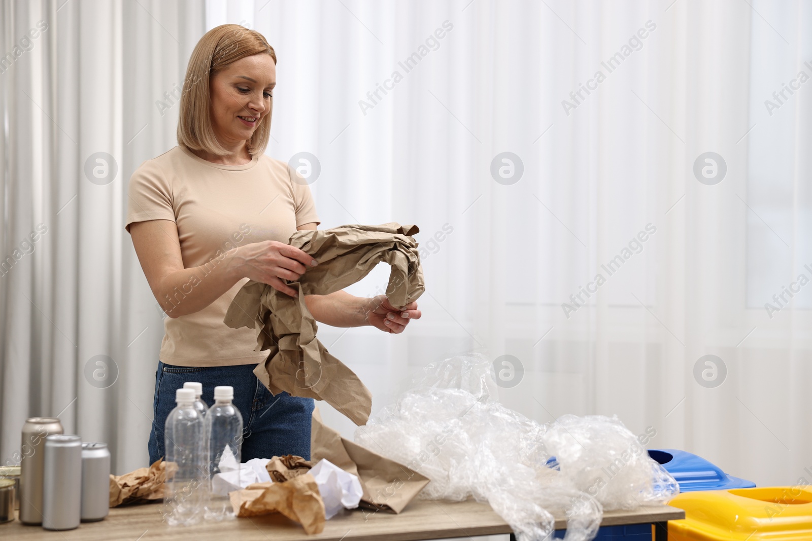 Photo of Smiling woman separating garbage in room. Space for text