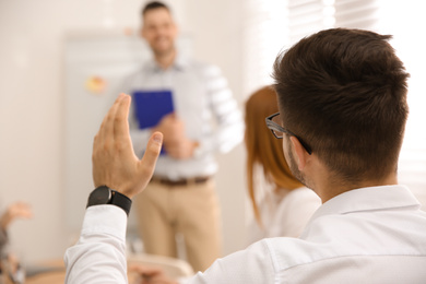 Young man raising hand to ask question at business training in conference room