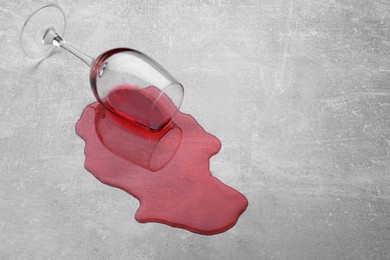 Photo of Glass with spilled red wine on light grey surface. Space for text