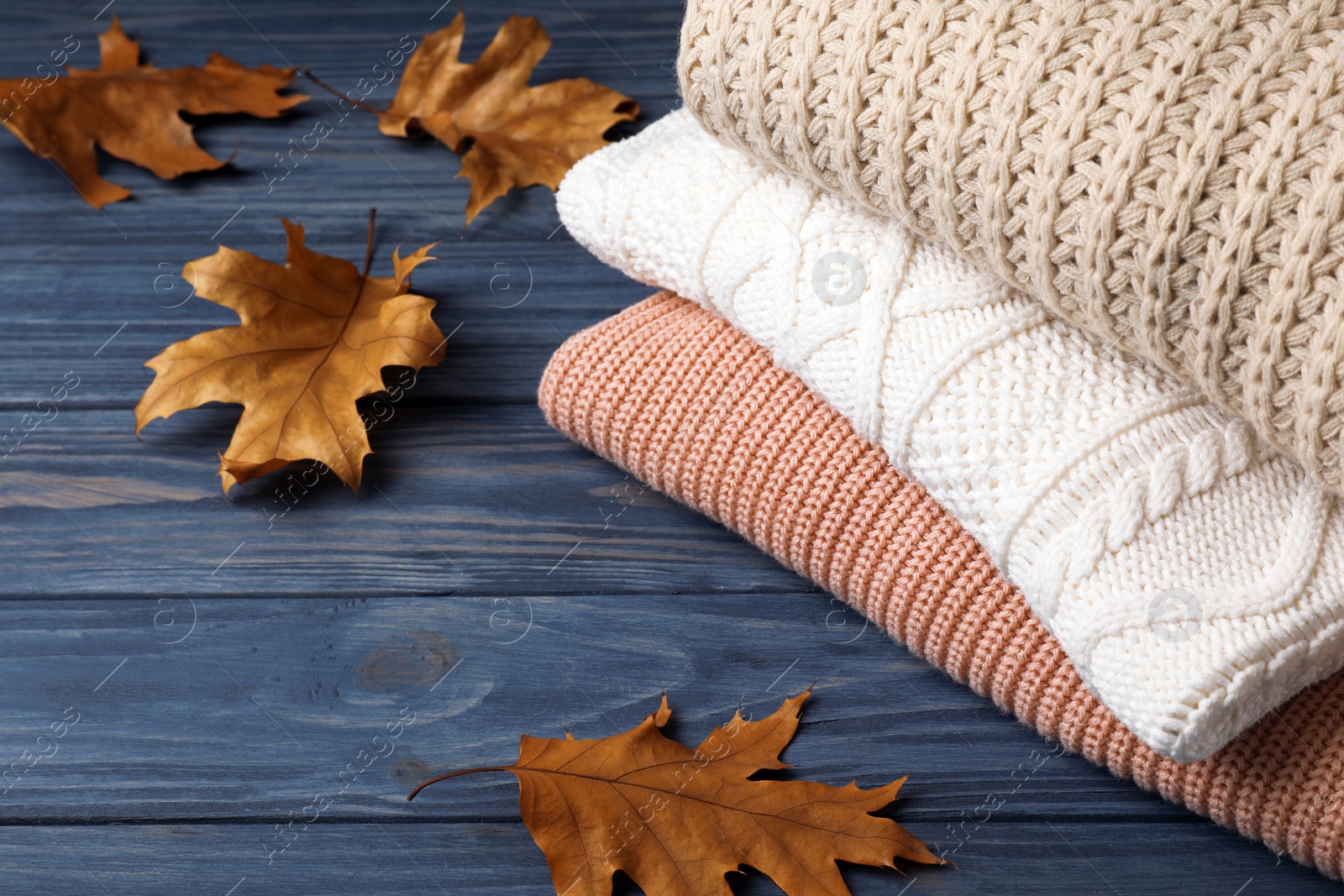 Photo of Stack of folded knitted sweaters and autumn leaves on table. Space for text