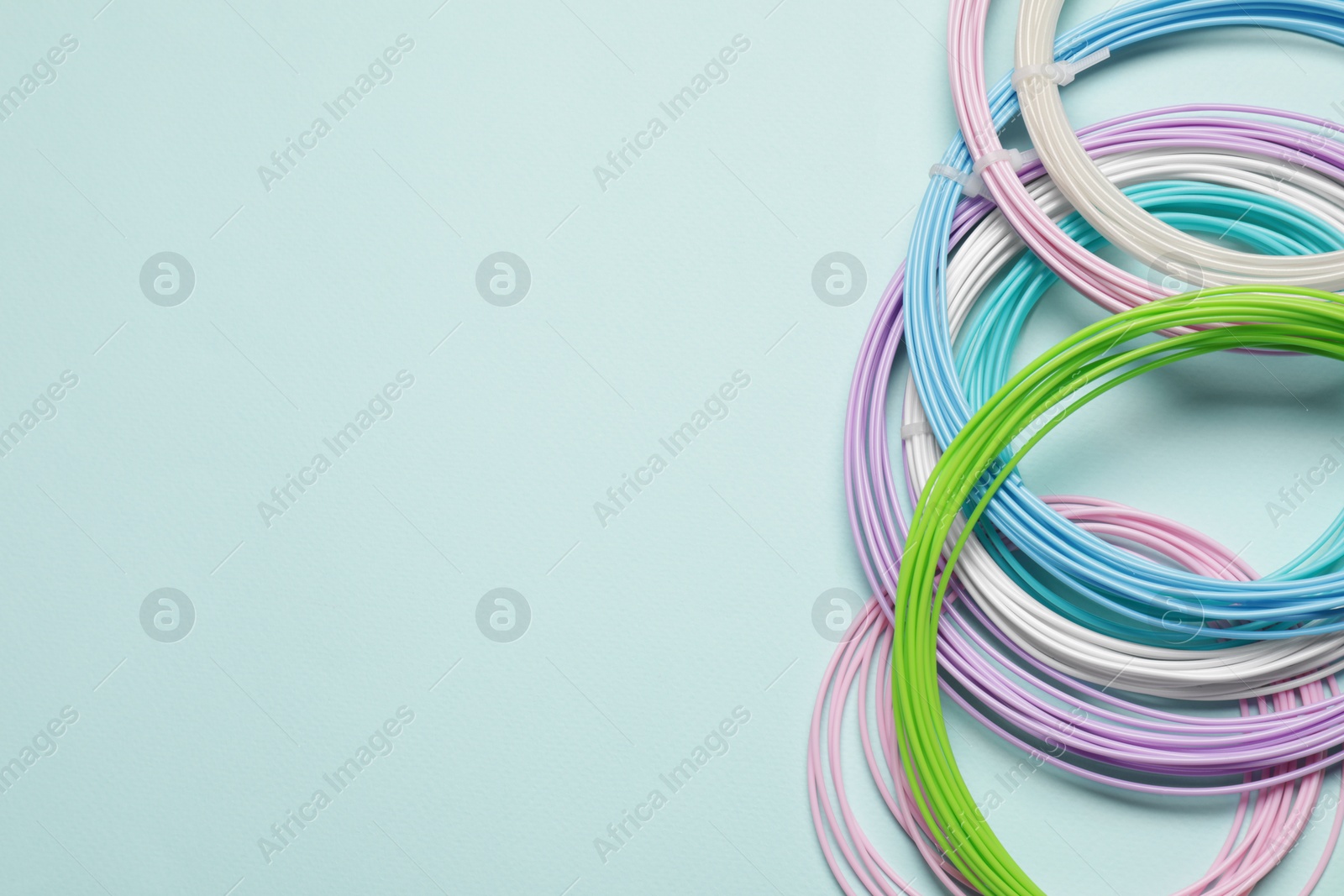 Photo of Colorful plastic filaments for 3D pen on light blue background, flat lay. Space for text