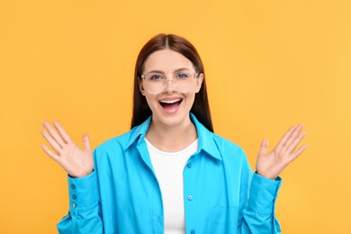 Portrait of emotional woman in stylish eyeglasses on orange background