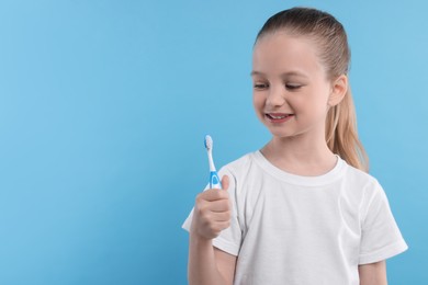 Photo of Happy girl holding toothbrush on light blue background. Space for text