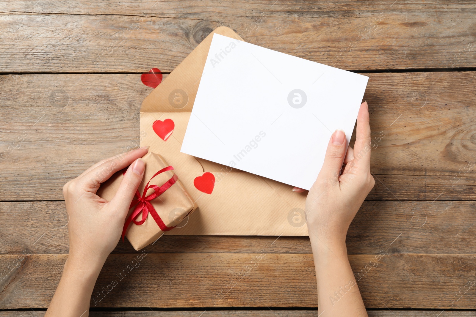 Photo of Woman holding blank greeting card and gift at wooden table, top view. Valentine's day celebration