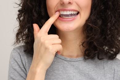 Photo of Young woman applying whitening strip on her teeth against light grey background, closeup