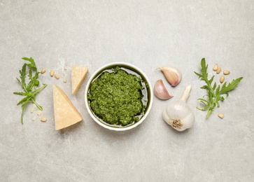 Bowl of tasty arugula pesto and ingredients on light table, flat lay