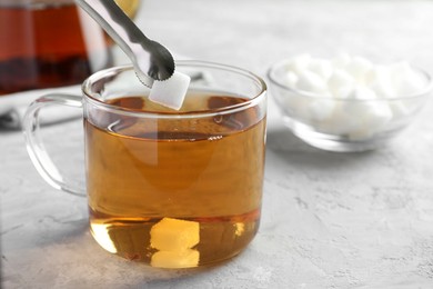 Adding sugar cube into cup of tea at grey textured table, closeup