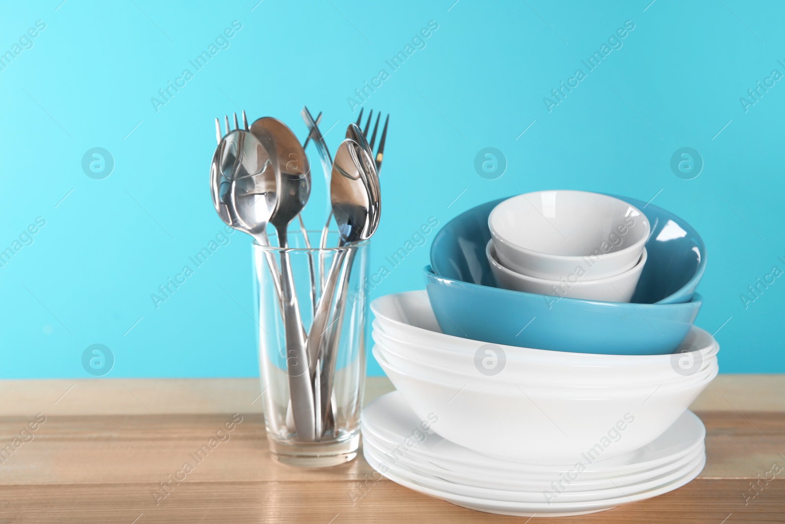 Photo of Set of clean dishes and cutlery on table against color background