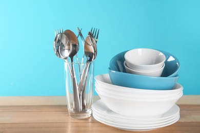 Set of clean dishes and cutlery on table against color background