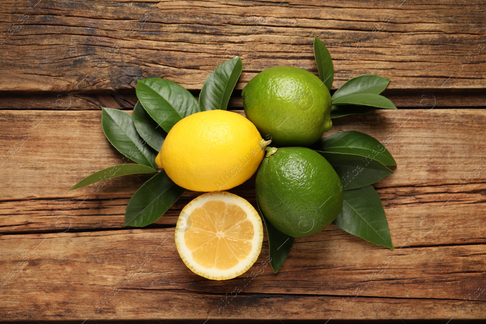 Photo of Fresh ripe lemons, lime and green leaves on wooden background, flat lay