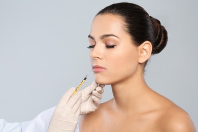 Photo of Young woman getting lips injection on grey background. Cosmetic surgery