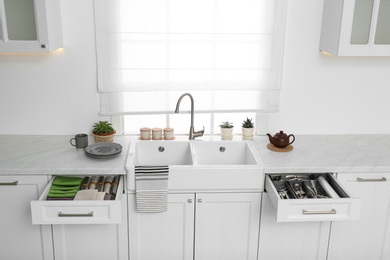 Photo of Open drawers with different utensils, towels and napkins in kitchen