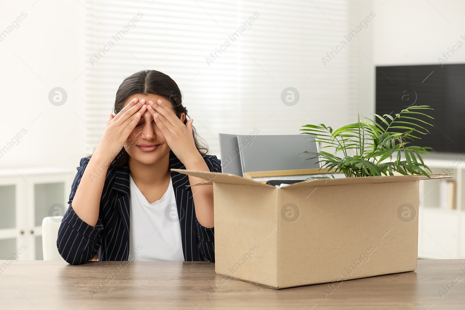 Photo of Unemployment problem. Frustrated woman with box of personal belongings at table in office