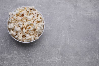 Photo of Bowl of tasty popcorn on grey table, top view. Space for text