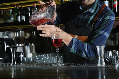 Photo of Barman pouring cocktail through strainer into glass at counter in pub, closeup