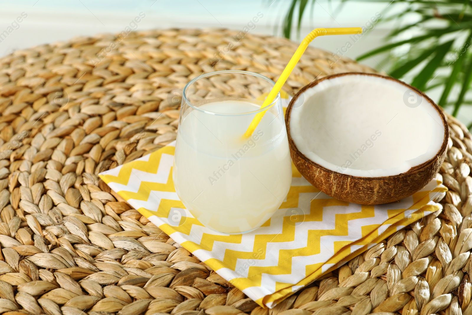 Photo of Composition with glass of coconut water on wicker table against blurred background