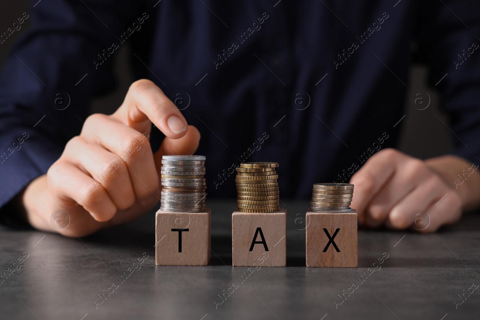 Photo of Taxes. Woman with wooden cubes and coins at grey table, closeup