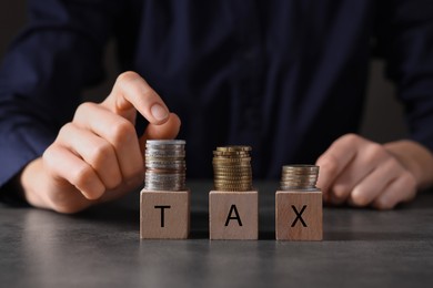 Taxes. Woman with wooden cubes and coins at grey table, closeup