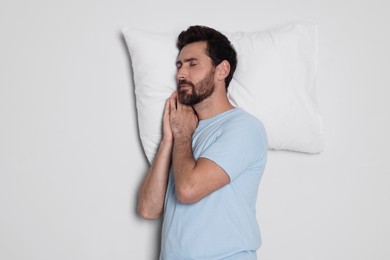 Sleepy handsome man with soft pillow on light grey background