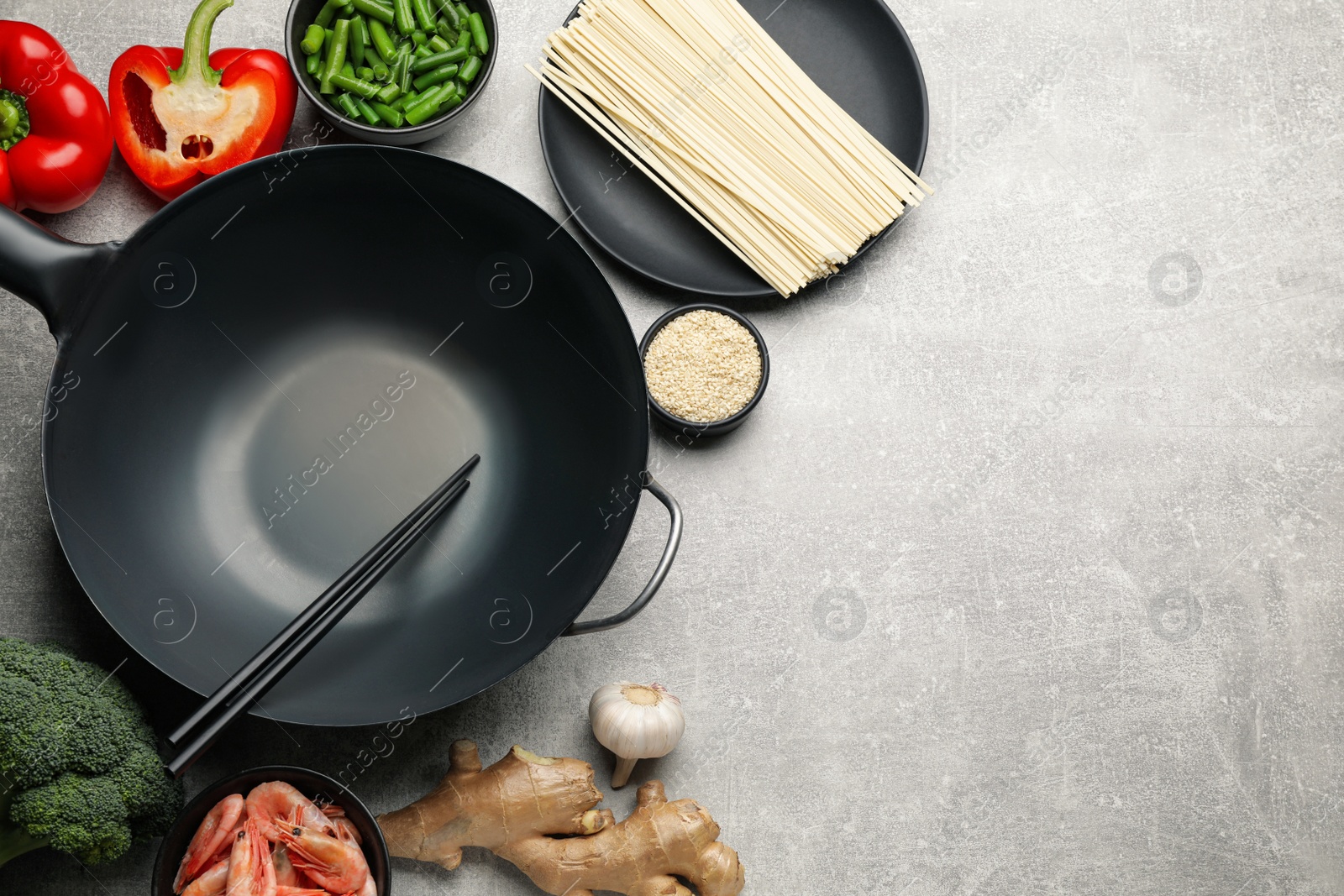 Photo of Empty iron wok with chopsticks and raw ingredients on light grey table, flat lay. Space for text