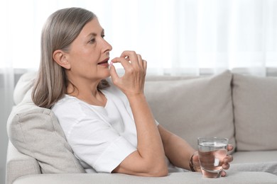 Senior woman with glass of water taking pill at home