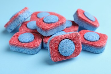 Photo of Many dishwasher detergent tablets on light blue background