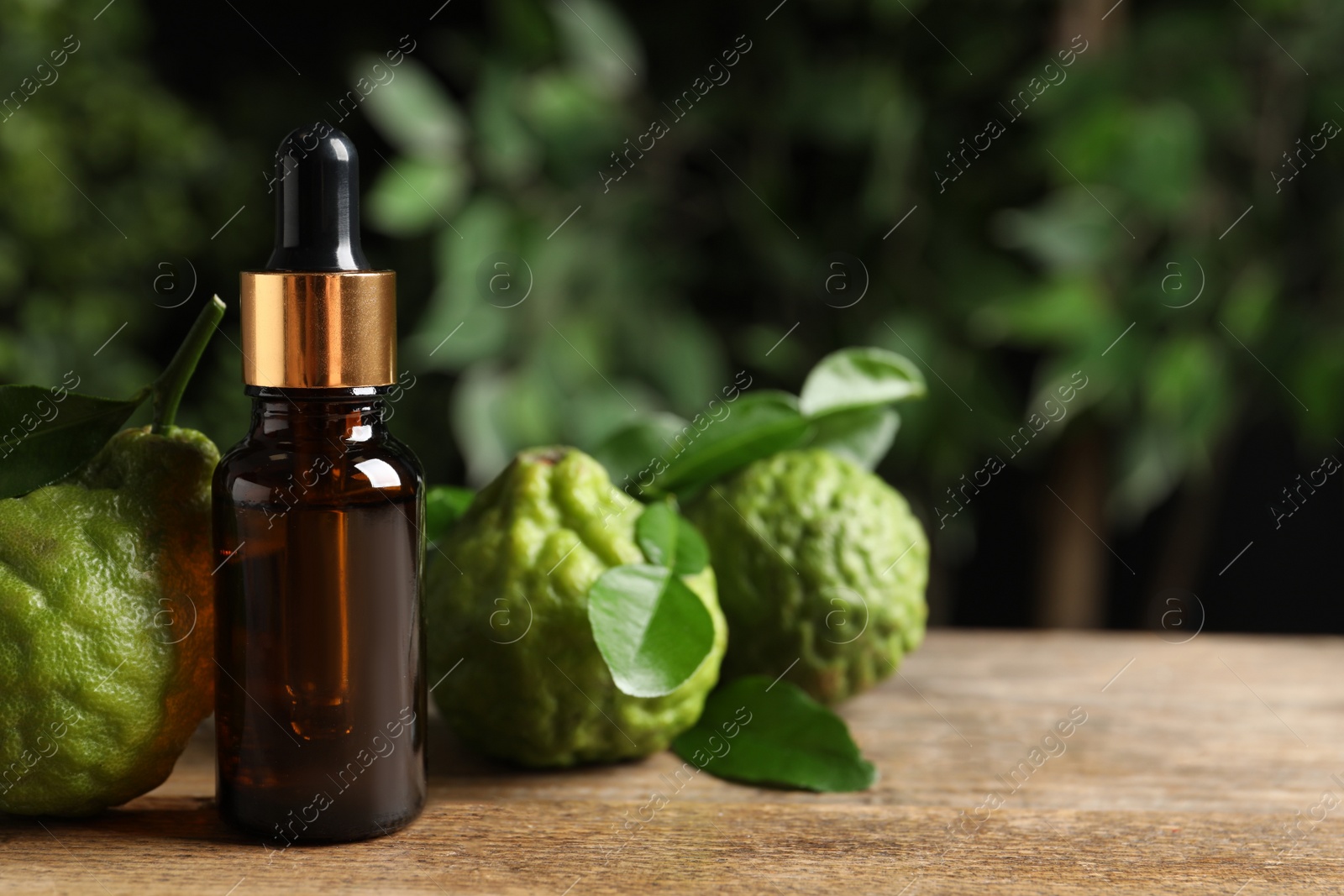 Photo of Glass bottle of bergamot essential oil and fresh fruits on wooden table. Space for text