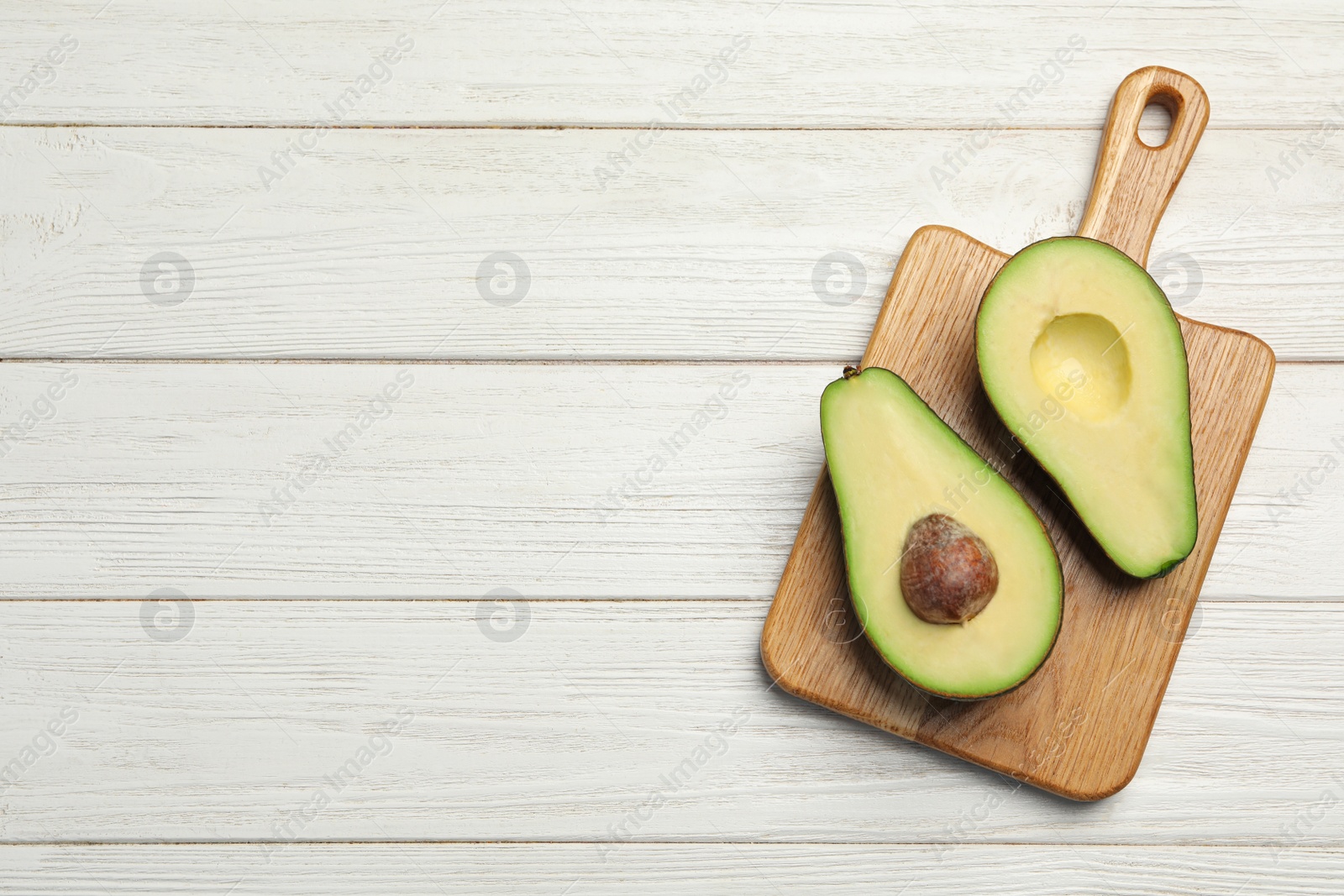 Photo of Halves of ripe avocado om white wooden table, top view. Space for text