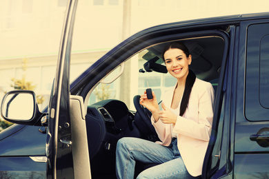 Image of Young woman with key sitting in car outdoors. Buying new auto