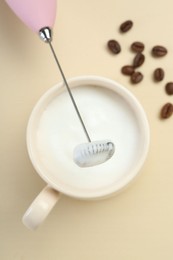 Mini mixer (milk frother), cup of whipped milk and coffee beans on beige background, flat lay